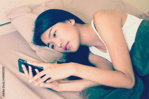 Closeup portrait of beautiful asian woman on bed while use smartphone, vintage color tone photo