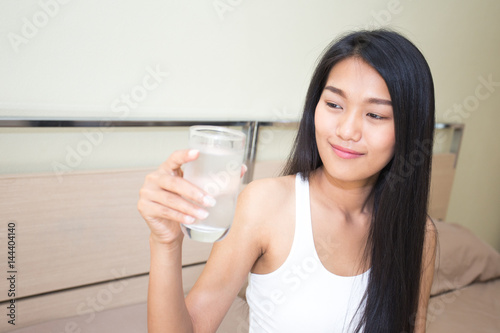 Beautiful asian woman with attractive smile while drinking water, Young woman portrait in bedroom.