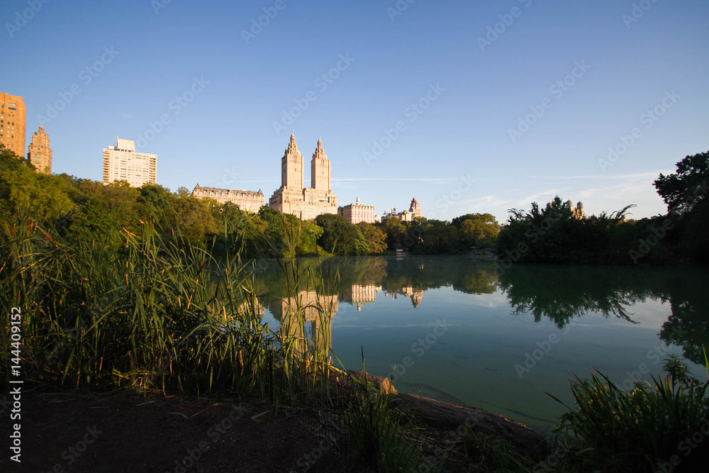 Buildings reflect in the lake at Central Park with blue sky, New York