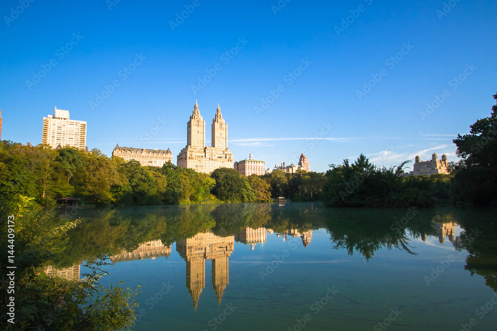 Buildings in Manhattan reflects on the lake at Central Park with blue sky, New York