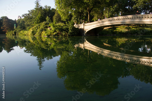 Bow bridge clearly reflects on the lake at Central Park with sky in summer