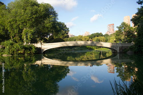 Bow bridge and trees clearly reflects on the lake at Central Park with sky