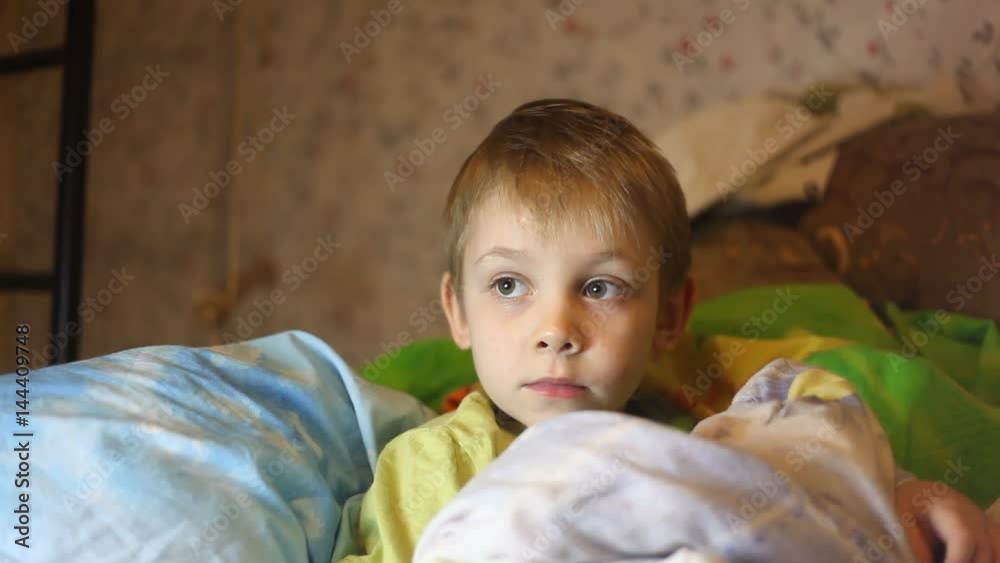 Sick little boy, lying in bed with a flu and a fever, watching TV in Russia Sick little boy, lying in bed with a flu and a fever, watching TV in Russia