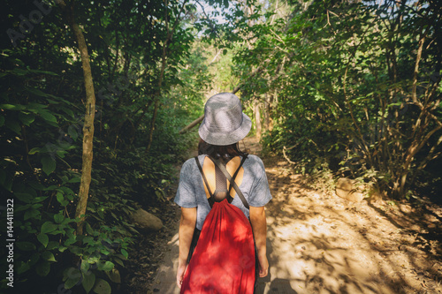 Back view of woman carry red backpack walking in the jungle