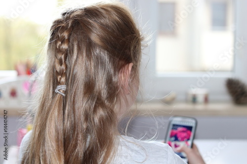 Young blond hair girl plays with mobile phone