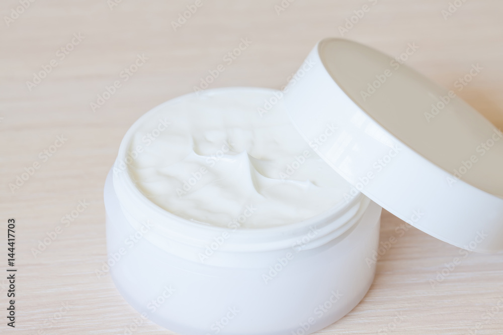 Body skin care and facial cream in cosmetics jar with opened cap on wooden background Body skin care and facial cream in cosmetics jar with opened cap on wooden background