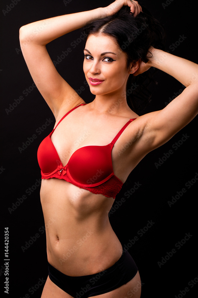 Portrait of sexy brunette woman in red and black underwear on a dark wall