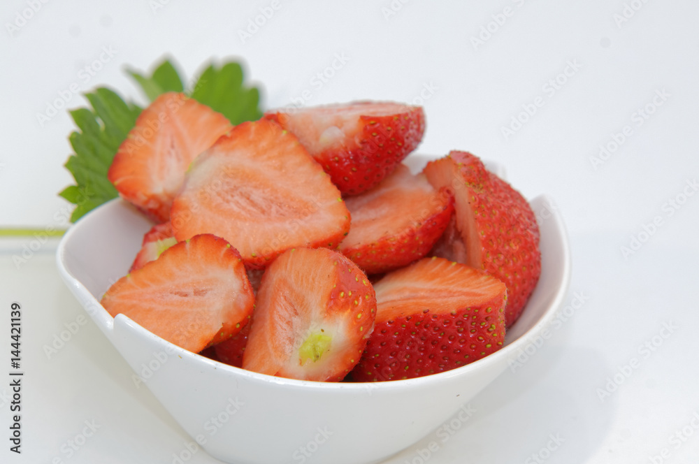 eine weiße Schale mit frischen halbierten Erdbeeren eine weiße Schale mit frischen halbierten Erdbeeren