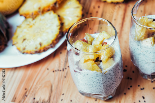 Glasses of chia seeds pudding with mango. Basil seeds in coconut milk with sliced pineapple and banana on a wooden table. A banch of bananas