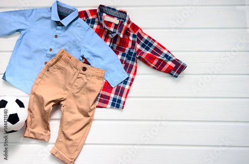 Baby boy clothing set (blue shirt, plaid red shirt and brown pant). Wish list or shopping overview for pregnancy and baby shower. View from above