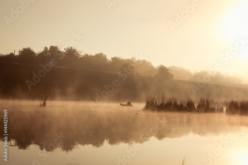 A misty morning by the lake. Small fishing boat at the lake. Space for text.