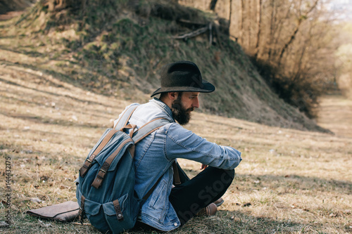 Bearded hipster Man traveler with hat and backpack sitting in the wood © Yevhenii Kukulka