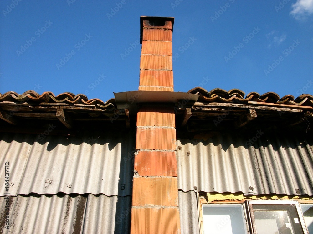 Schornstein aus rotem Backstein eines alten Haus mit Wellblechfassade