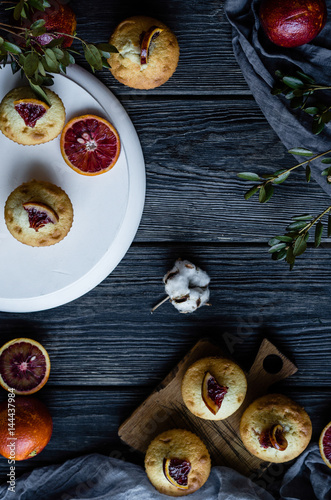 Muffins with blood oranges on a white wooden stand with green leaves, cloth and wooden desk on a black background photo