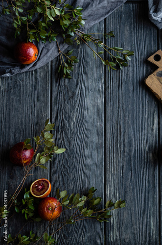 Food frame with blood oranges with green leaves on a black wooden background