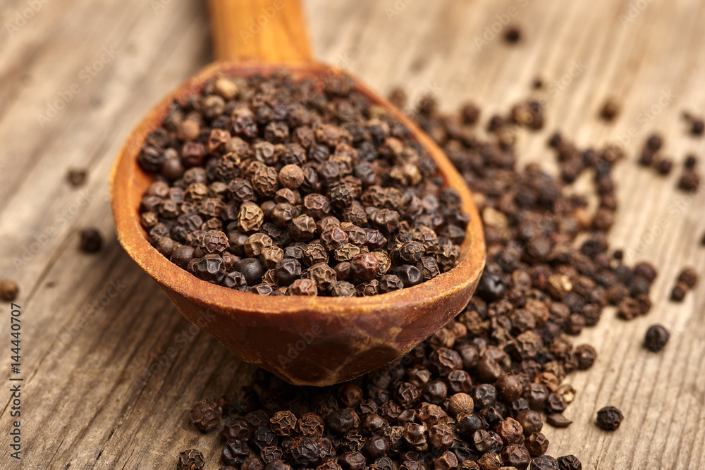Closeup black pepper whole in wooden spoon on old wooden background Closeup black pepper whole in wooden spoon on old wooden background