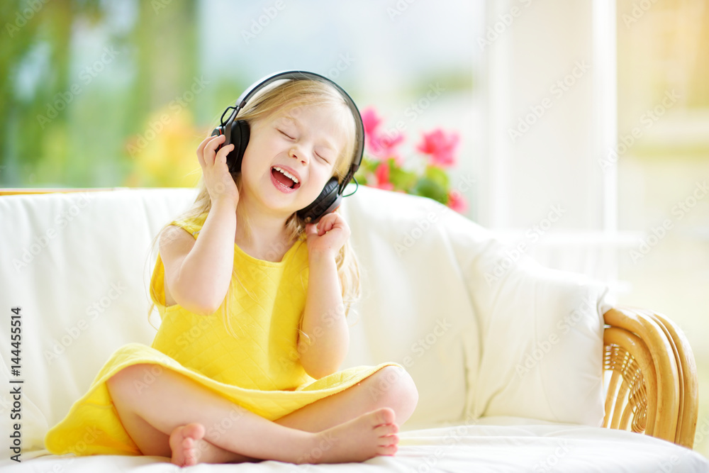 Cute girl wearing huge wireless headphones. Pretty child listening to the music. Schoolgirl having fun listening to kid's songs at home. Cute girl wearing huge wireless headphones. Pretty child listening to the music. Schoolgirl having fun listening to kid's songs at home.