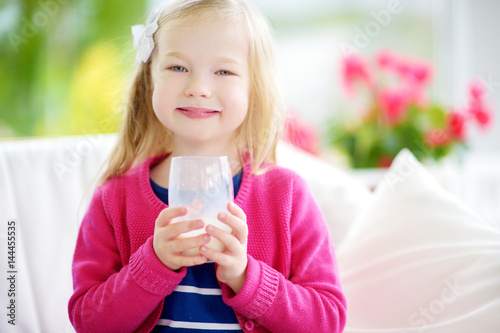 Cute little girl drinking fresh organic milk at sunny summer day. Healthy nutrition for children.