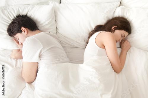 Top view of young indifferent man and woman sleeping separately back to back in bed after quarrelling, difficulties in relationships, problems in sex life, family conflicts, falling out of love