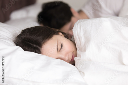 Couple having a restful sleep, young pretty lady lying on pillow under covering in comfortable white bed, looking peaceful and serene, soft healthy sleep on weekend and good dreams