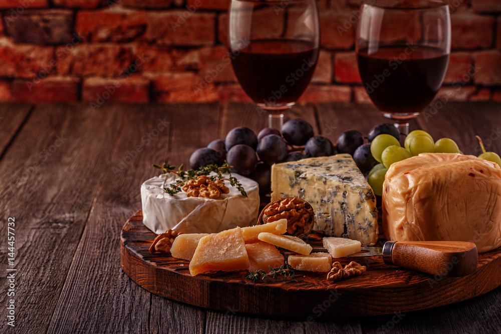 Cheese, nuts, grapes and red wine on wooden background.