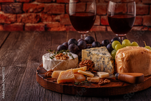 Cheese, nuts, grapes and red wine on wooden background.