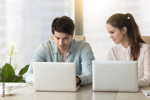 Fotografie Young lady taking inquisitive glance, sneak peek at laptop screen of male collea