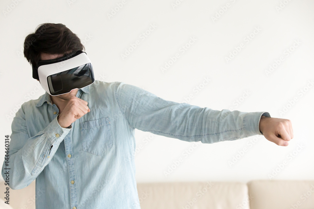 Young gamer wearing virtual reality glasses for gaming applications, boxing or fighting. Using mobile apps with innovative virtual technology. Augmented reality gamer device. Man playing in vr headset Young gamer wearing virtual reality glasses for gaming applications, boxing or fighting. Using mobile apps with innovative virtual technology. Augmented reality gamer device. Man playing in vr headset
