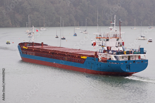 Cargo ship making its way in heavy rain up the Truro river near Malpas guided by a pilot boat en route to the river Fal