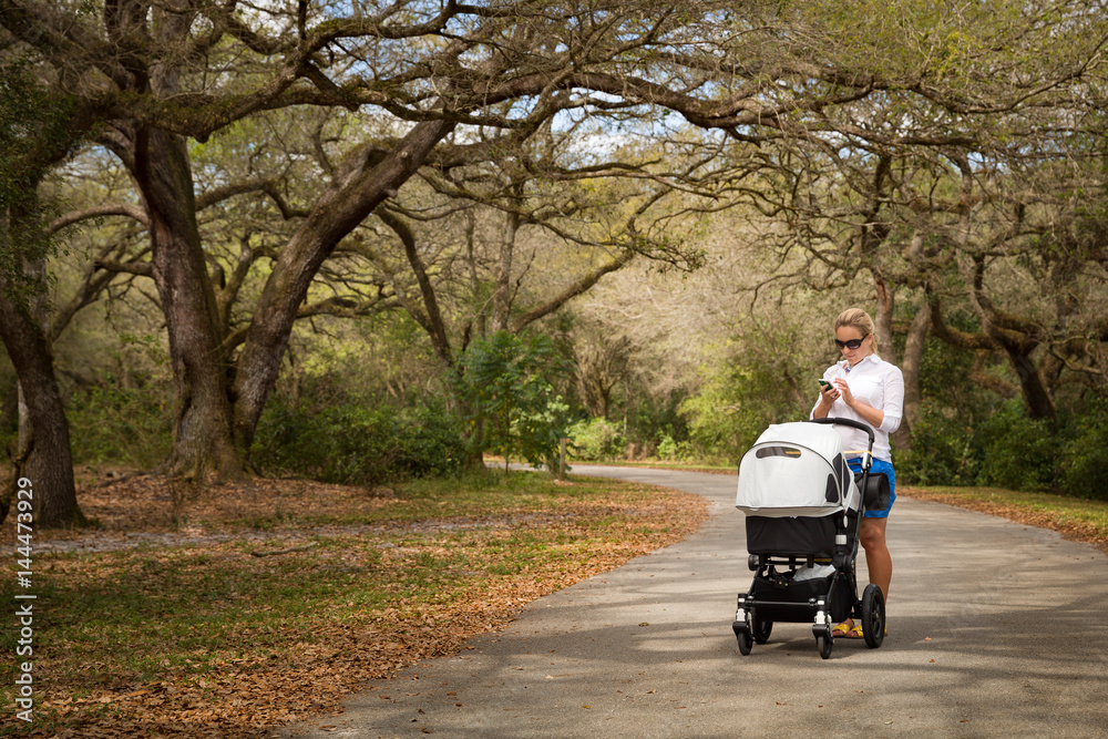 Young woman walking in the park with baby stroller. Happy mother with child in the carriage. Girl with a pram outdoors in the big park. Young woman walking in the park with baby stroller. Happy mother with child in the carriage. Girl with a pram outdoors in the big park.