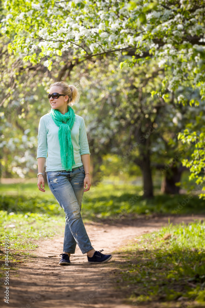 Young woman standing in the blooming apple garden and looking into distance. Enjoying spring day outdoors. Girl walking in the park. Young woman standing in the blooming apple garden and looking into distance. Enjoying spring day outdoors. Girl walking in the park.