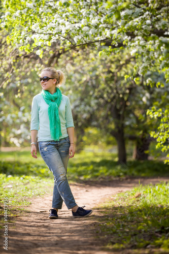 Young woman standing in the blooming apple garden and looking into distance. Enjoying spring day outdoors. Girl walking in the park.