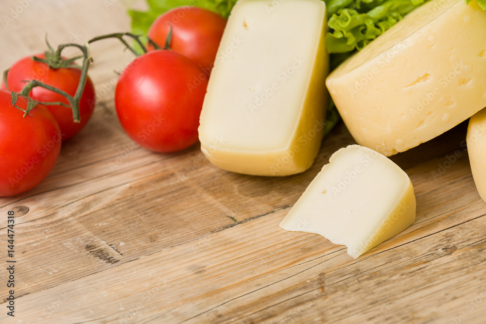 Cut cheese heads on wooden board served with tomatoes and fresh salad. Serving French homemade cheese. Food concept Cut cheese heads on wooden board served with tomatoes and fresh salad. Serving French homemade cheese. Food concept