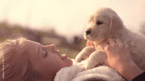 White Golden Retriever Puppy Cuddling Up with Owner Girl Laying on Lawn in Park Outdoors Summer Spring Day Kissing Hugging Petting