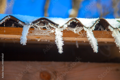 Icicles of snow hanging from a roof in a winter sunny day. Snow crystals are visible