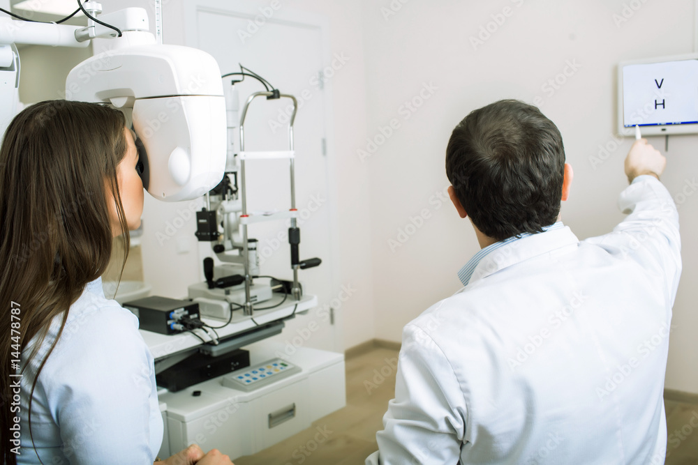 Fototapeta premium patient woman having her eyes examined by an optometrist using phoropter, in ophthalmology clinic.