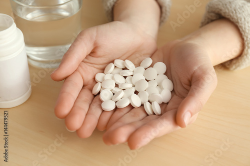 Female hands with pills and glass of water on wooden background, closeup