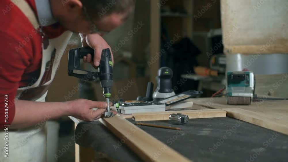 Carpenter making a hole in the wooden plank with a drill in the workshop Carpenter making a hole in the wooden plank with a drill in the workshop