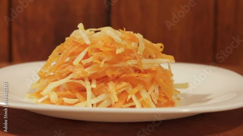 Vegetable salad of carrot and cabbage in white plate on wooden background close up. Vegetarian healthy salad in vegetable oil
