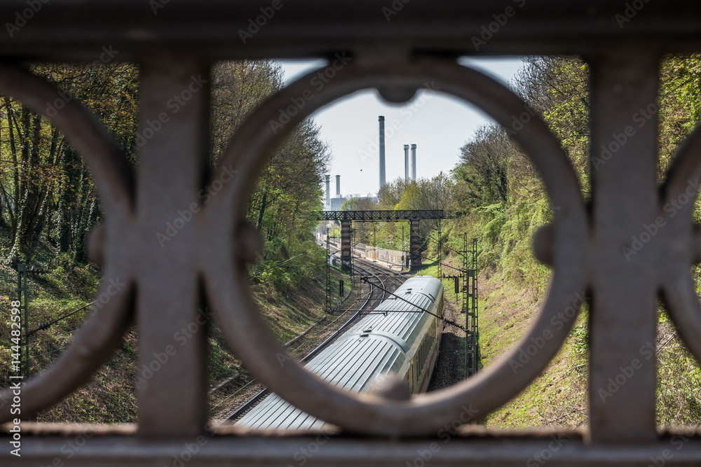 Zugverkehr in München mit Heizkraftwerk Süd im Hintergrund - durch Brückengeländer gesehen Zugverkehr in München mit Heizkraftwerk Süd im Hintergrund - durch Brückengeländer gesehen