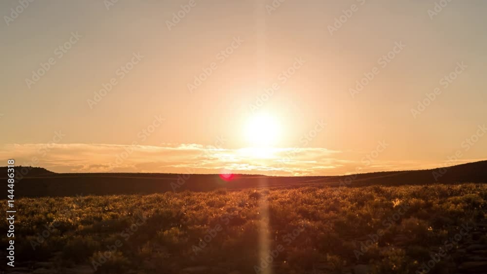 A peaceful static sunrise timelapse of slow moving scattered clouds with golden light and sun flare in a landscape with wide open vistas