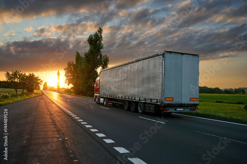 Truck driving toward the setting sun on the road in the countryside