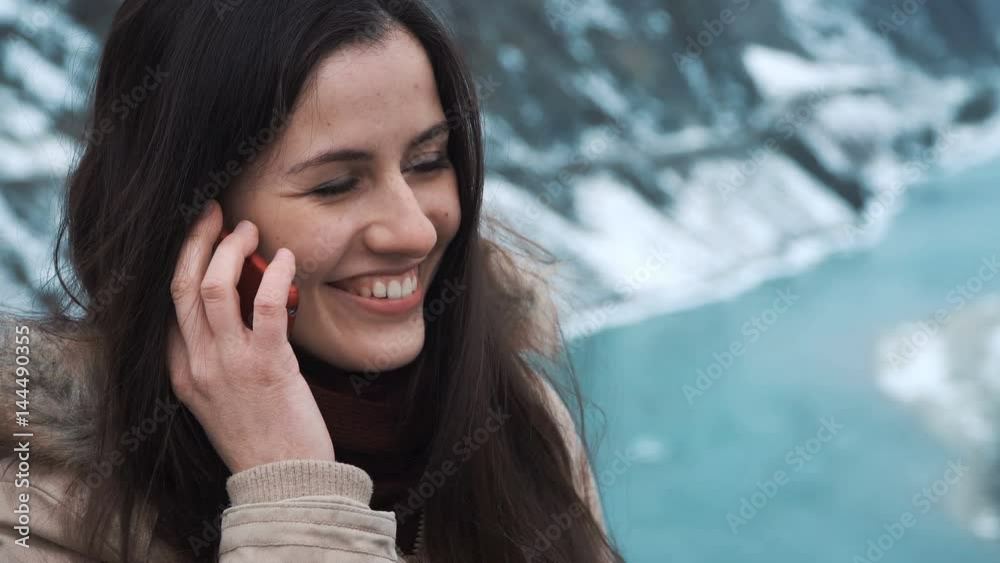 A beautiful girl is calling on the smartphone. Sharing emotions from adventures or traveling in the winter in the mountains A beautiful girl is calling on the smartphone. Sharing emotions from adventures or traveling in the winter in the mountains