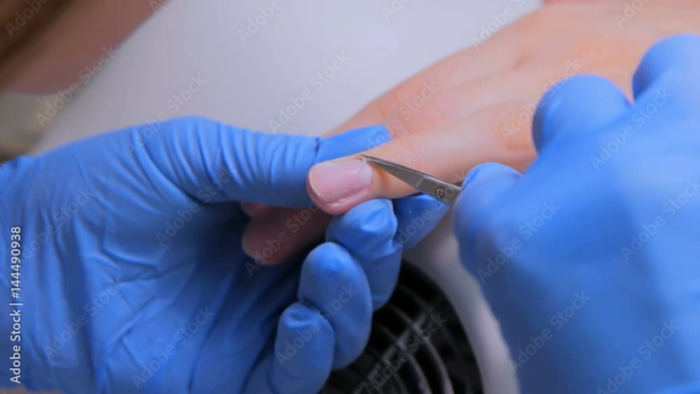 Closeup finger nail care by manicure specialist in beauty salon. Manicurist clear cuticle with professional scissors for manicure Closeup finger nail care by manicure specialist in beauty salon. Manicurist clear cuticle with professional scissors for manicure