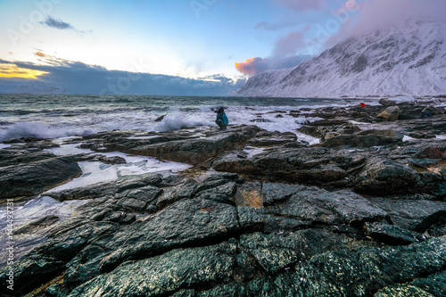 Travel photographer doing pictures in ancient stones on the shores of cold Norwegian Sea at evening time. Lofoten islands. Beautiful Norway landscape.