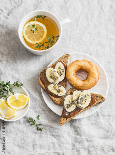 Banana sandwich with chia seeds, donuts and green tea with lemon and thyme on a light background, top view. Delicious breakfast or snack