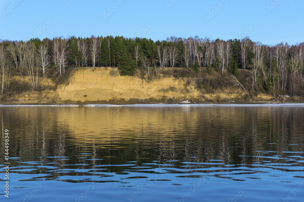 A steep bank of the river. A view from the water with a mirror image. River Ob, Novosibirsk, Russia. 8 April 2017