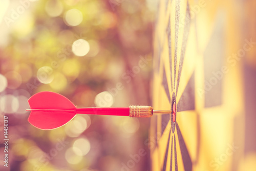 Red dart arrow in the center of dartboard. Blur and bokeh in sunrise time background. Warm vintage effect style