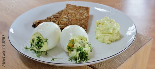 Plate with tro eggs, rye bread, curry salad and cress