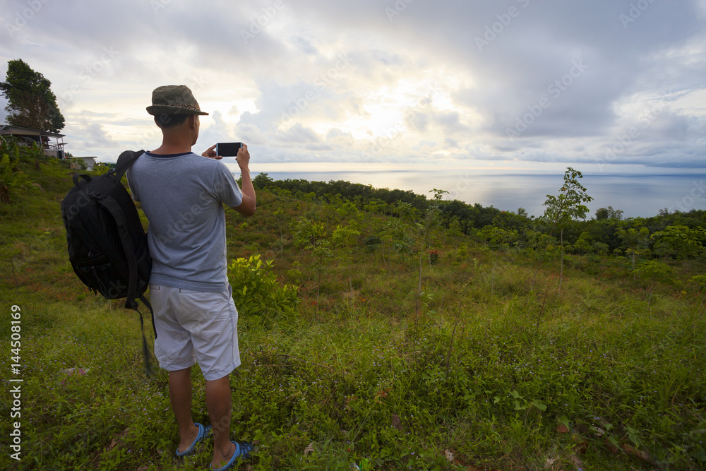 Traveler man with backpacker standing take a photo landscape tropical sea view sunset andaman sea. Traveler man with backpacker standing take a photo landscape tropical sea view sunset andaman sea.
